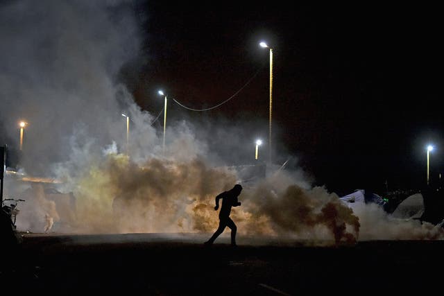 A refugee flees police tear gas near the entrance to the Jungle camp in Calais