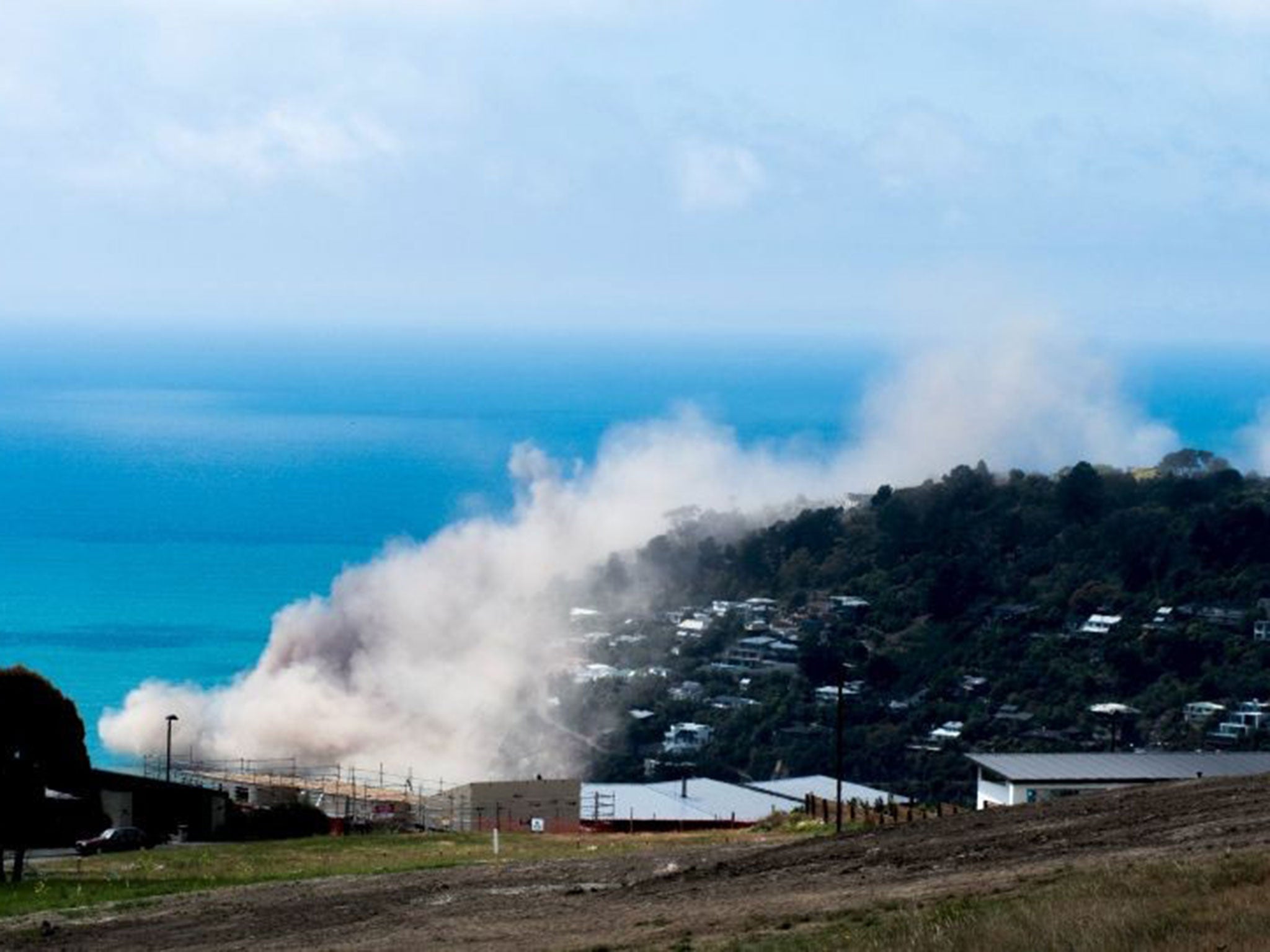 Dust and debris rise above houses after a cliff collapsed due to an earthquake on the Whitewash Head area