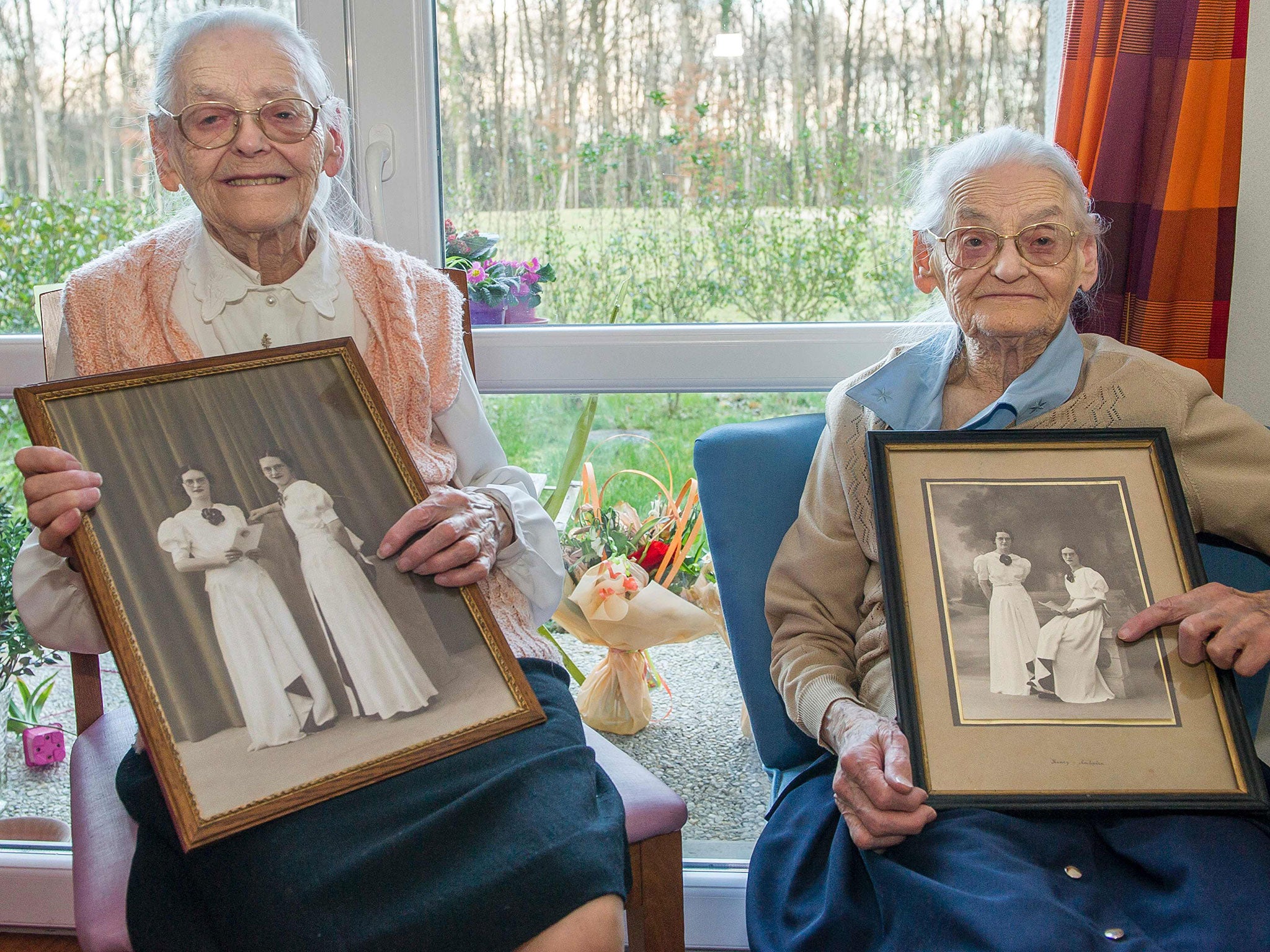 Centenary twins, Paulette Olivier, left, and Simone Thiot, right, pose with an old picture of themselves at the age of 20, inside their room at the Ephad 'Les Bois Blancs'