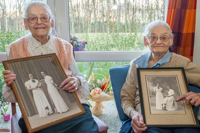 Centenary twins, Paulette Olivier, left, and Simone Thiot, right, pose with an old picture of themselves at the age of 20, inside their room at the Ephad 'Les Bois Blancs'