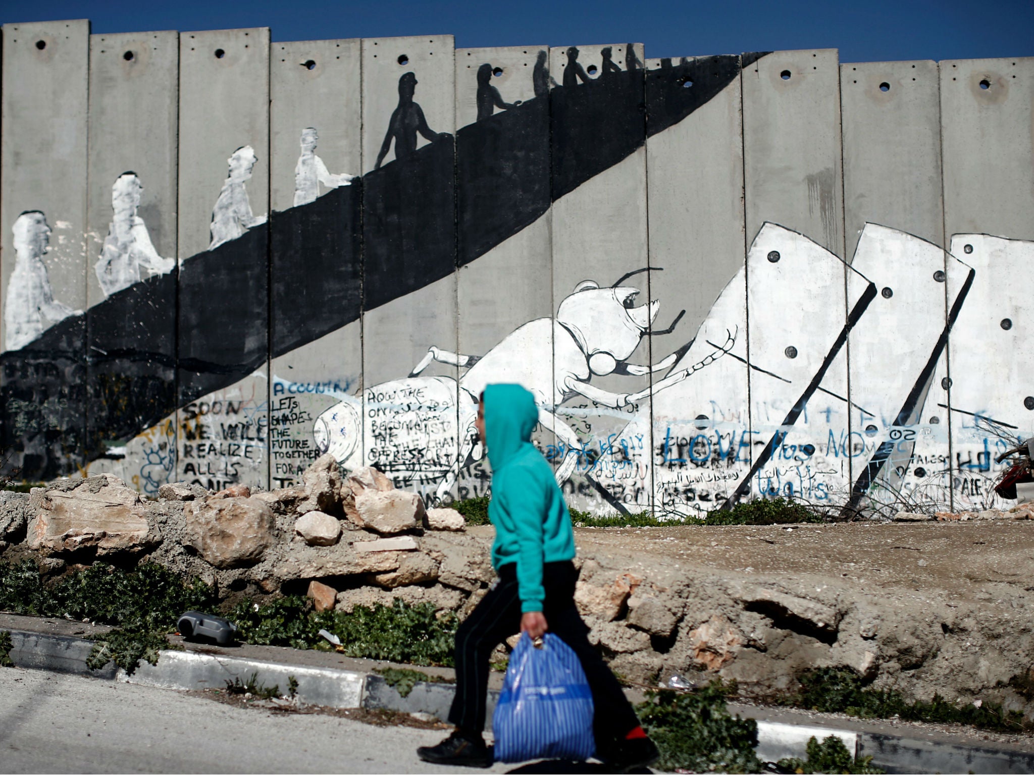 A Palestinian boy walks past graffiti painted on Israel's controversial separation barrier in the Aida refugee camp situated inside the West Bank town of Bethlehem, on February 12, 2016