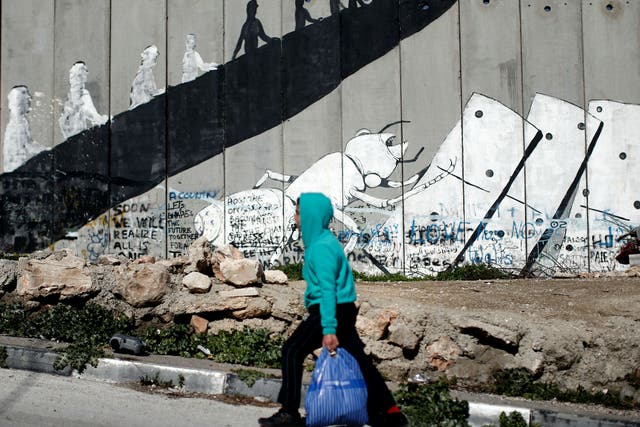 A Palestinian boy walks past graffiti painted on Israel's controversial separation barrier in the Aida refugee camp situated inside the West Bank town of Bethlehem, on February 12, 2016