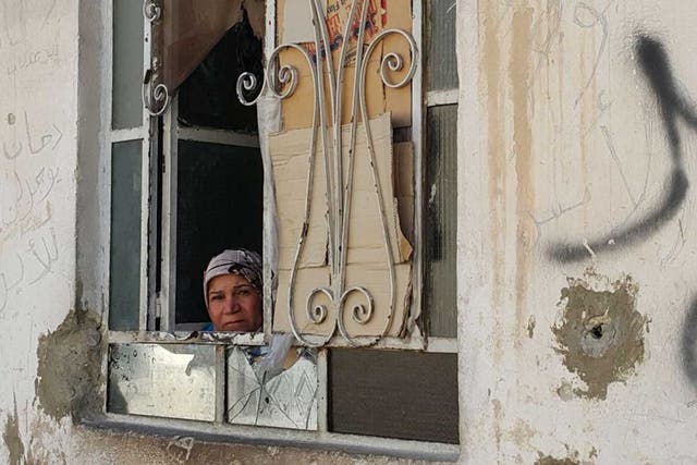 A woman peers out of her window in the battered district of Damascus where a fragile ceasefire holds