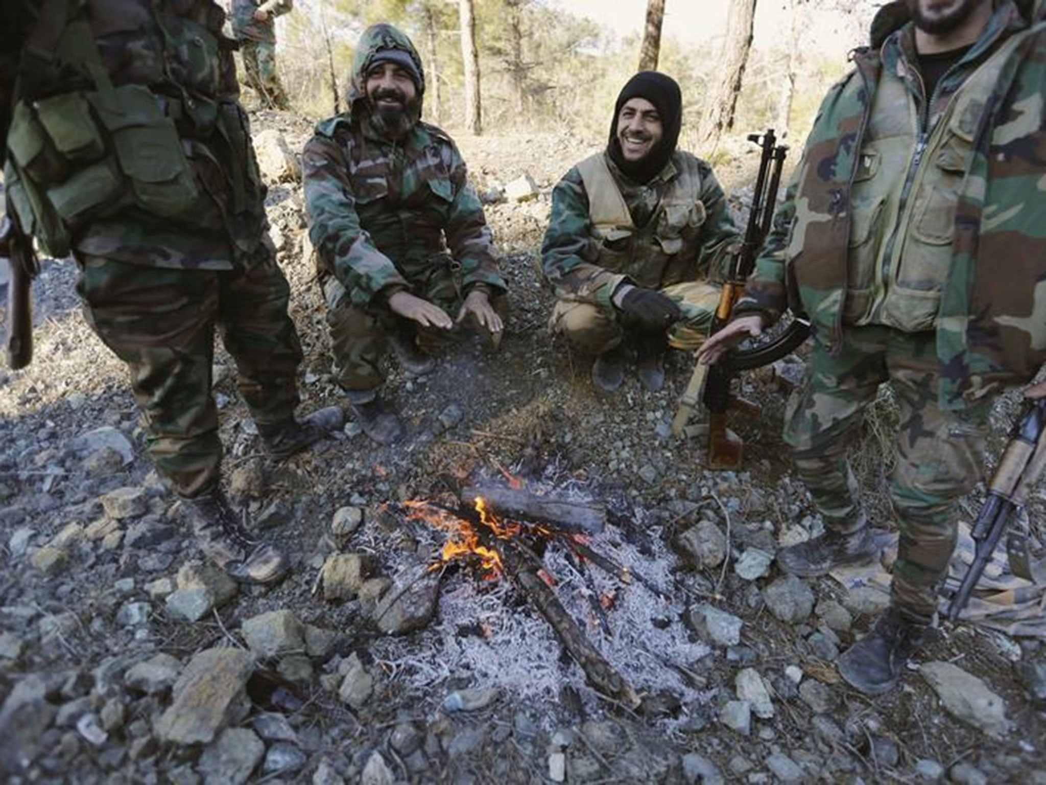 Forces loyal to Syria's President Bashar al-Assad warm themselves around a fire beside a road leading to the town of Rabiya