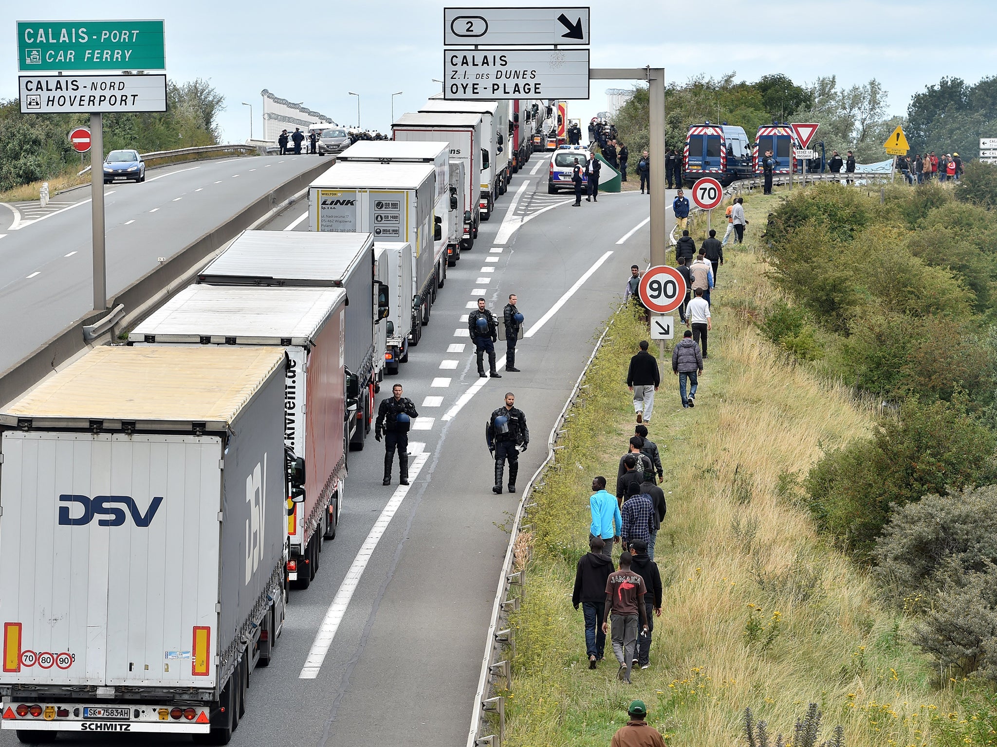 Police officers try to prevent migrants from climbing aboard trucks travelling to Britain, outside Calais last year