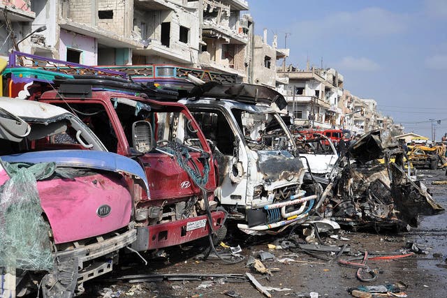 Wrecked buildings and vehicles at the site of twin car bombings that killed at least 57 people in the Syrian city of Homs
