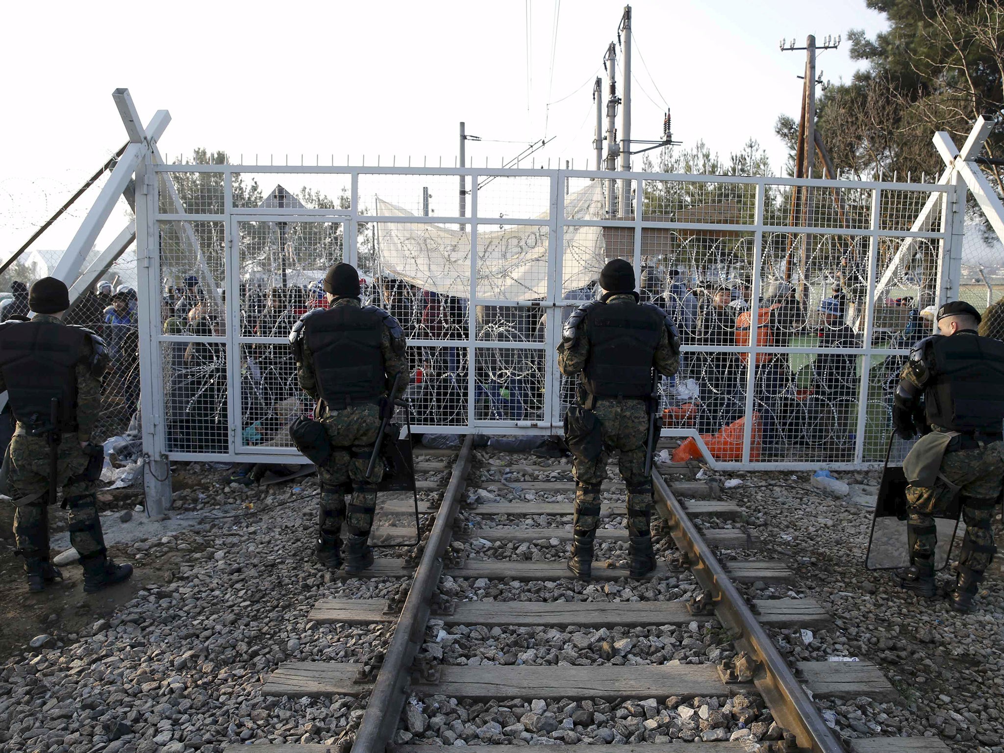 Macedonian policemen stand in front of a gate over rail tracks as migrants wait behind at the Greek-Macedonian border, after additional passage restrictions imposed by Macedonian authorities left hundreds of them stranded near the village of Idomeni, Greece.