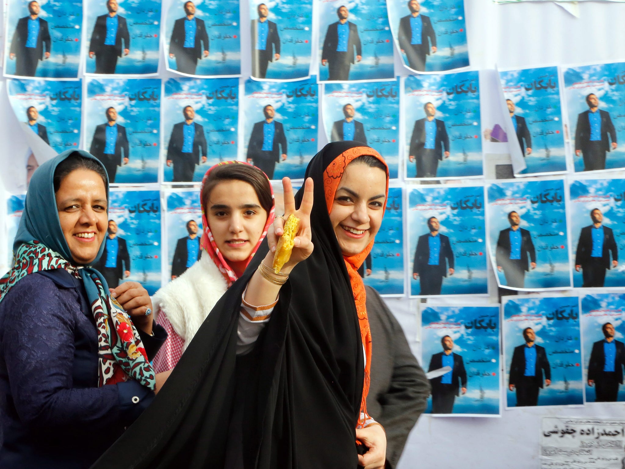 An Iranian woman flashes the victory sign as she walks next to the electoral posters for the parliamentary election