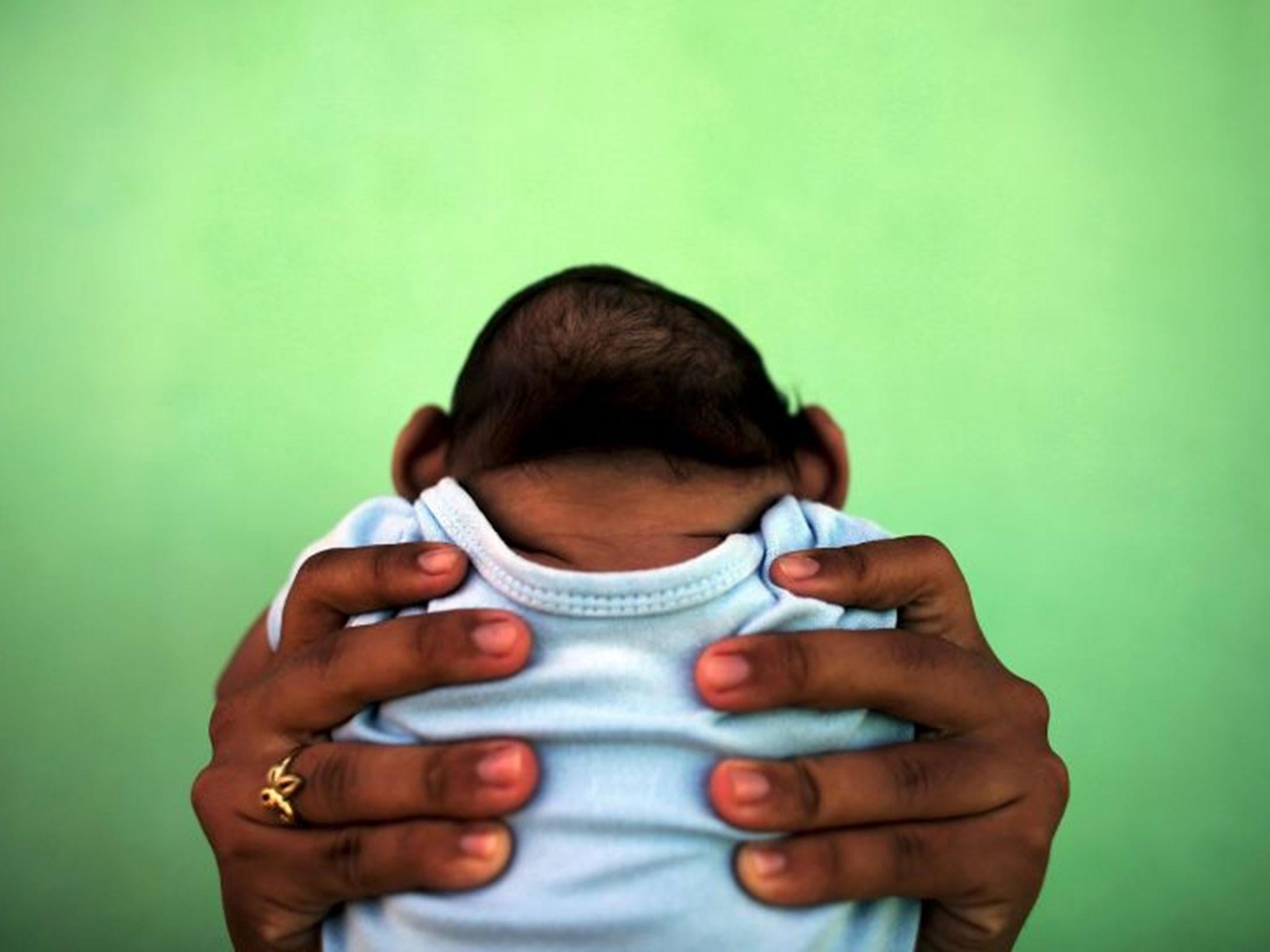 A woman holds her son who is 4-months old and born with microcephaly, which can be caused by Zika, in front of their house in Olinda, Brazil