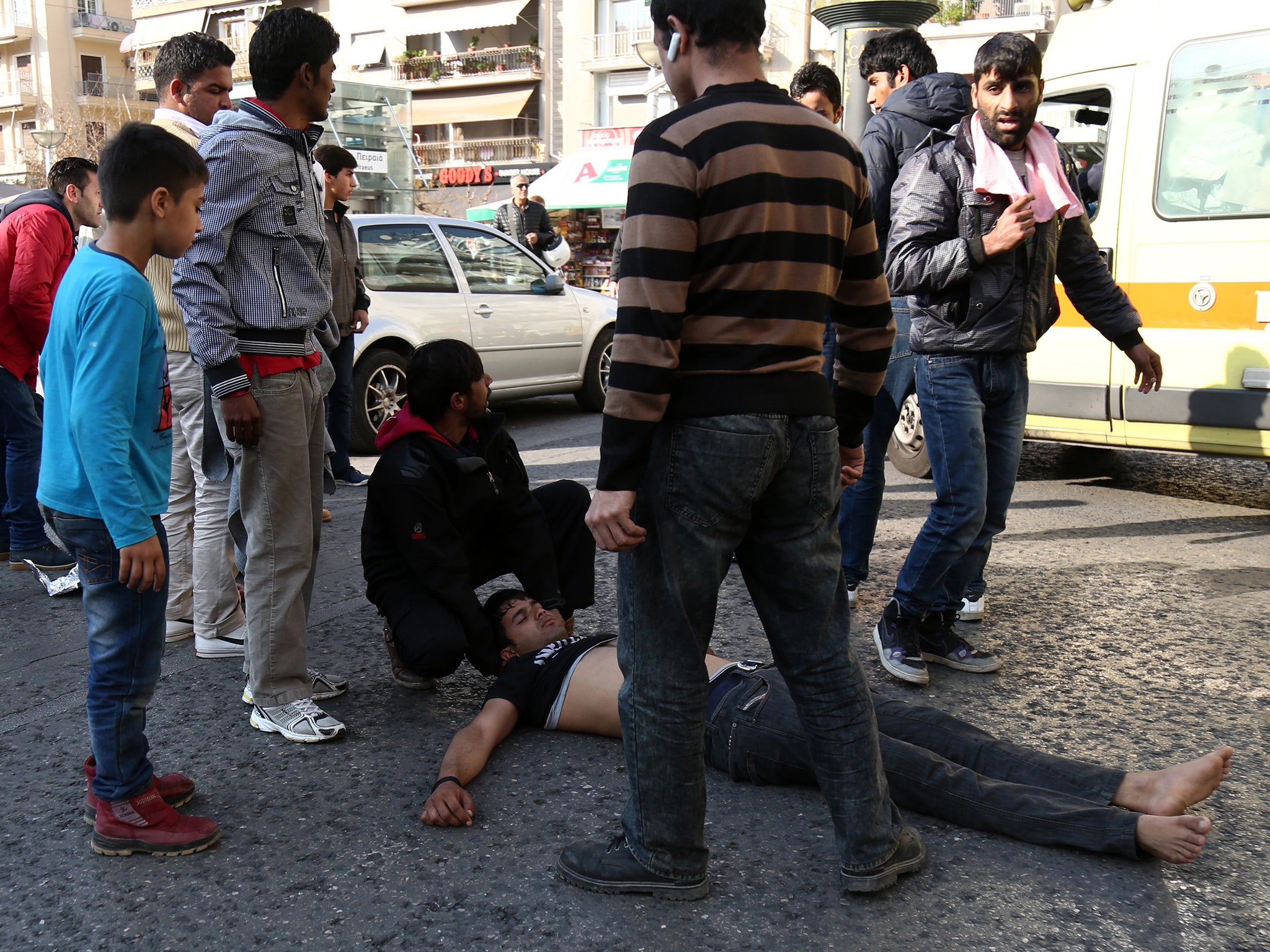 A Pakistani man, who tried to commit suicide by hanging himself with twisted lengths of fabric from a tree, lies on the street as other migrants wait for the ambulance in central Athens' Victoria Square