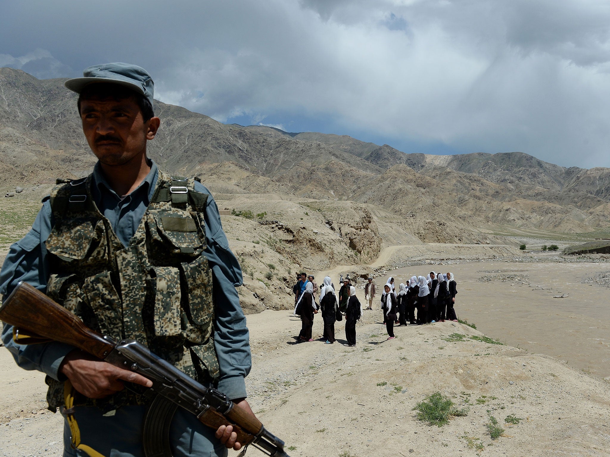 An Afghan policeman stands guard as schoolgirls wait for a bus in Baghlan province