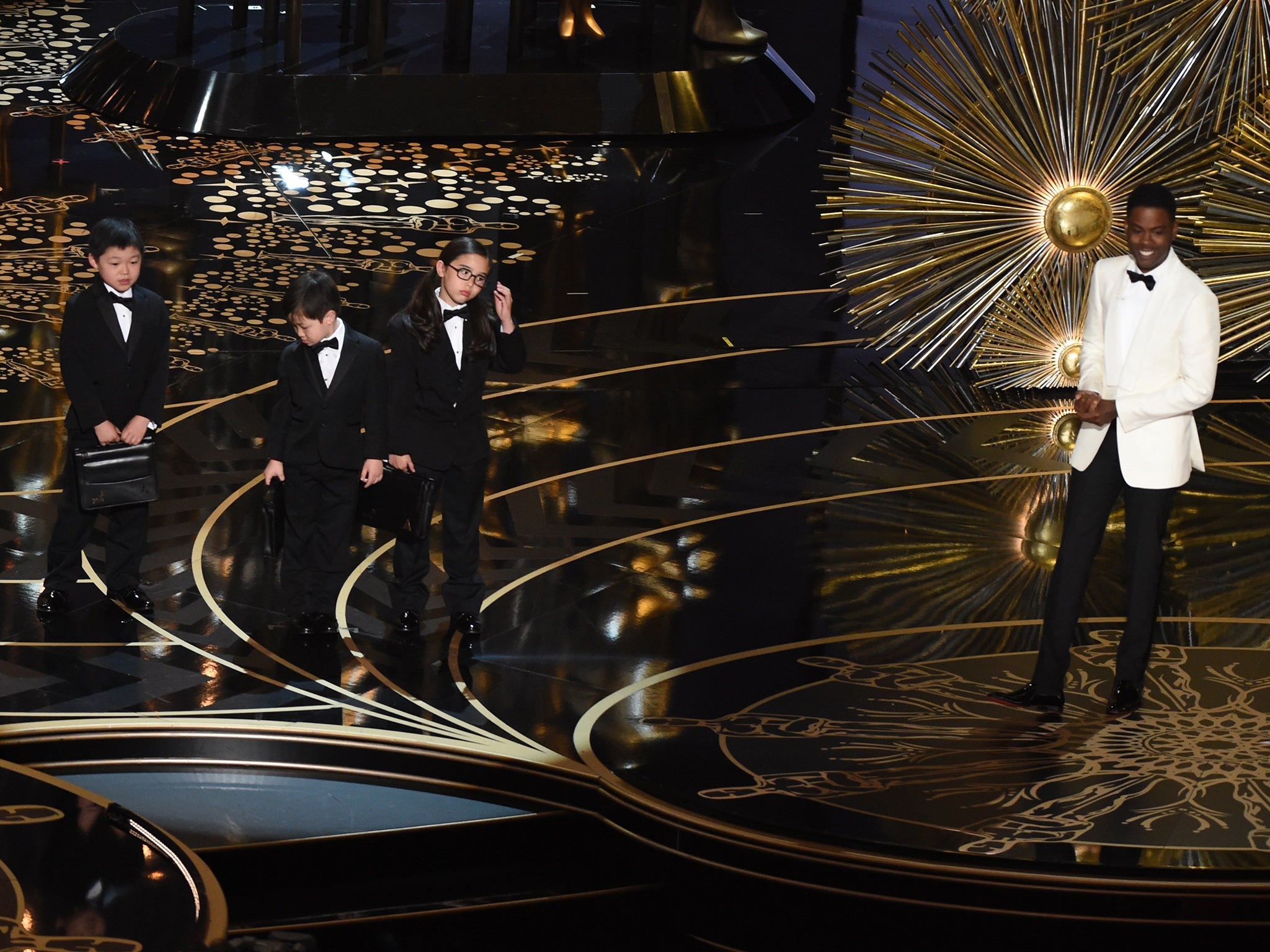 Actor Chris Rock presents children representing accountants from PricewaterhouseCoopers on stage at the Oscars