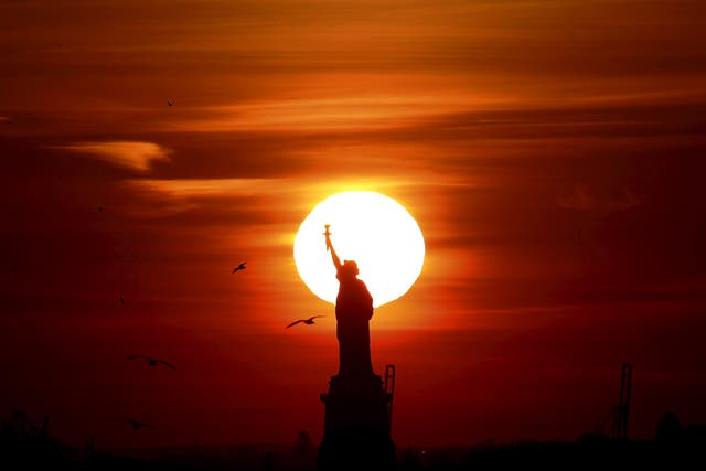 The sun sets behind the Statue of Liberty in New York's Harbor as seen from the Brooklyn borough of New York