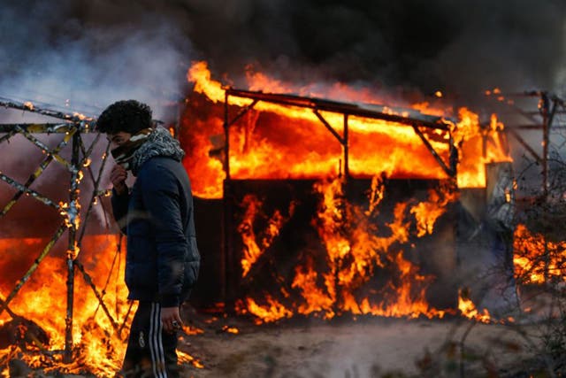 A refugee watches a shelter burn during the start of the expulsion at the Jungle camp