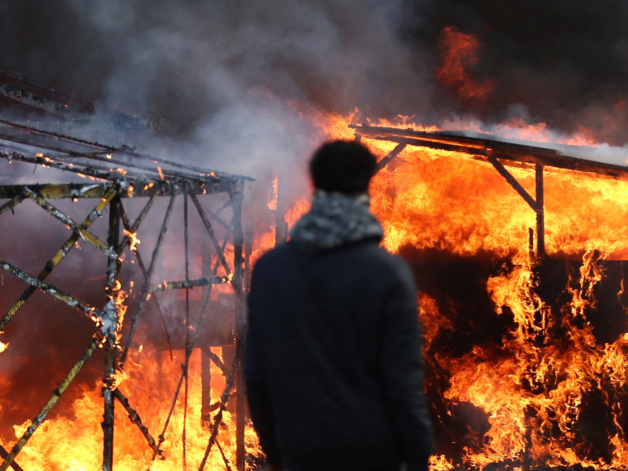 Migrants watch a hut burn as police officers clear part of the 'jungle' migrant camp on February 29, 2016 in Calais, France
