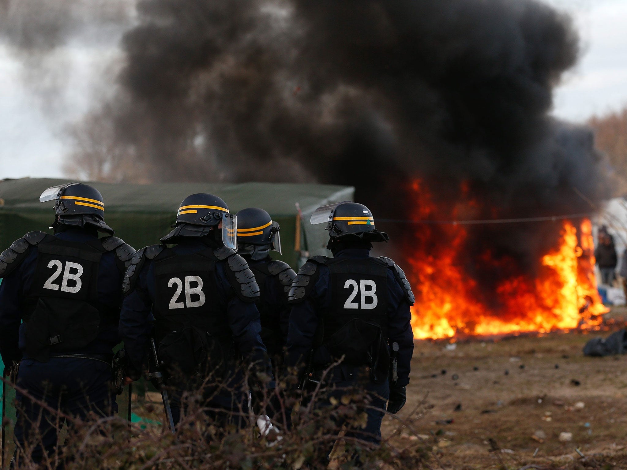 French riot police in front of a burning shelter at the start of the demolition of a part of the Jungle migrant camp in Calais, France, 29 February 2016.