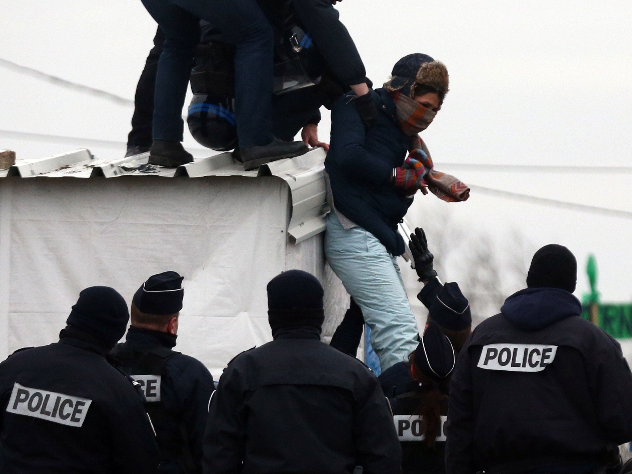 Police detain a woman who had threatened to cut her wrist as she was removed from the roof of a hut as they cleared the "jungle" migrant camp on March 01, 2016 in Calais, France.