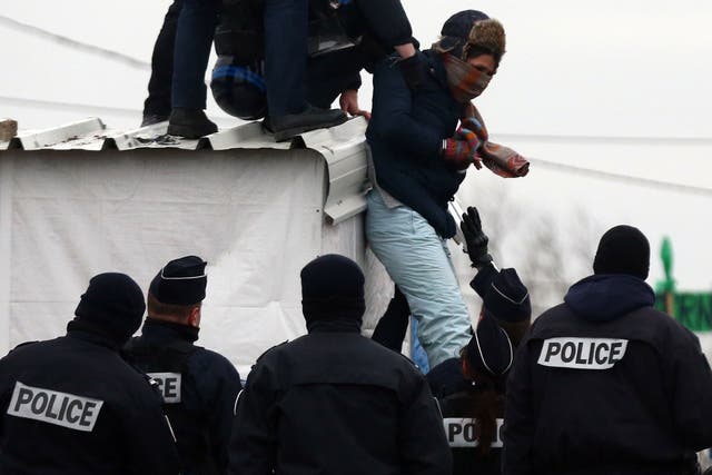 Police detain a woman who had threatened to cut her wrist as she was removed from the roof of a hut as they cleared the "jungle" migrant camp on March 01, 2016 in Calais, France.