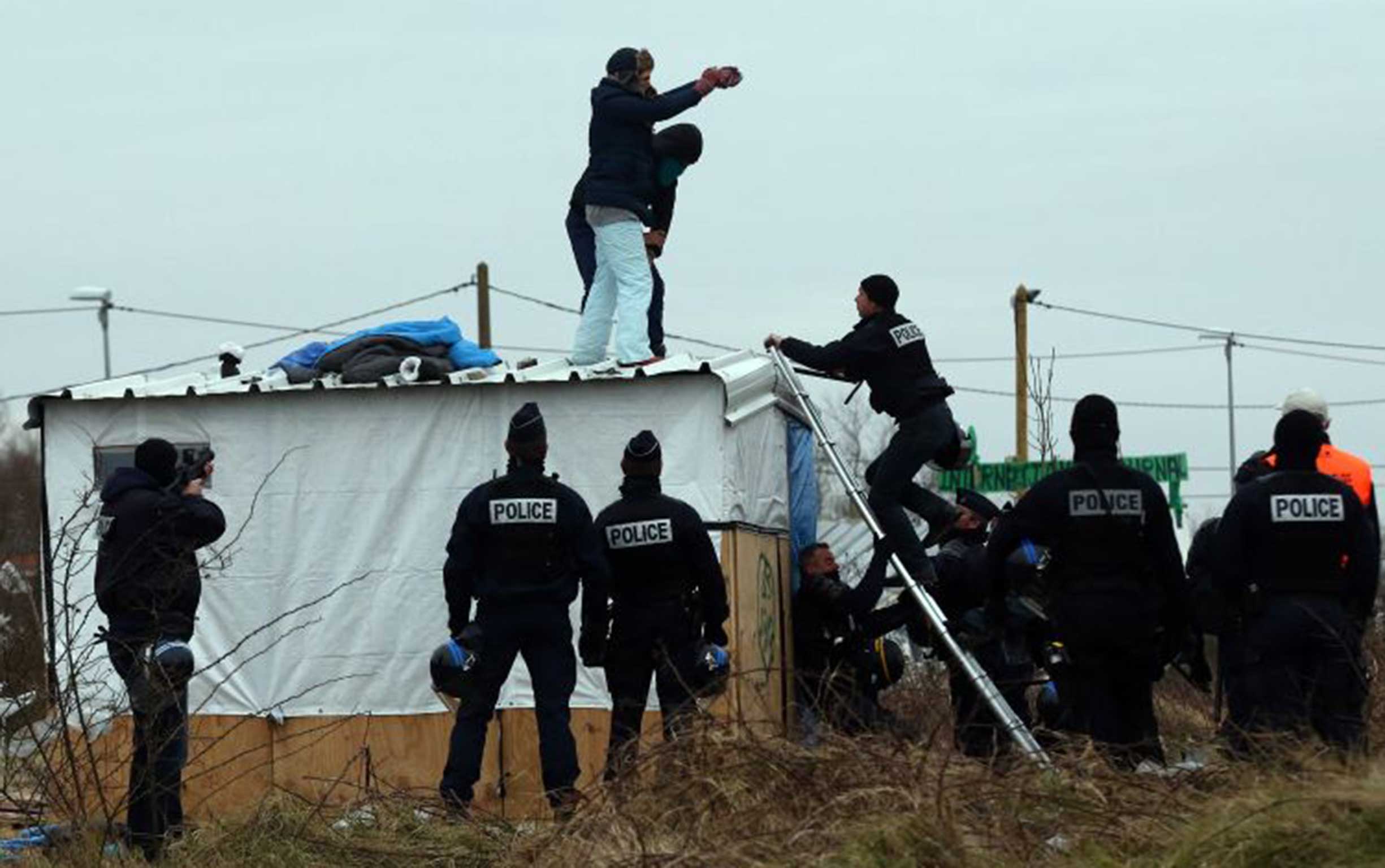 French police prepare to remove a woman, who threatened to cut her wrists, and a man from the top of a hut as they clear the Jungle camp in Calais