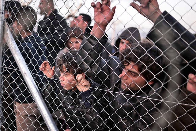 Refugees look through a fence at the Greek-Macedonian border