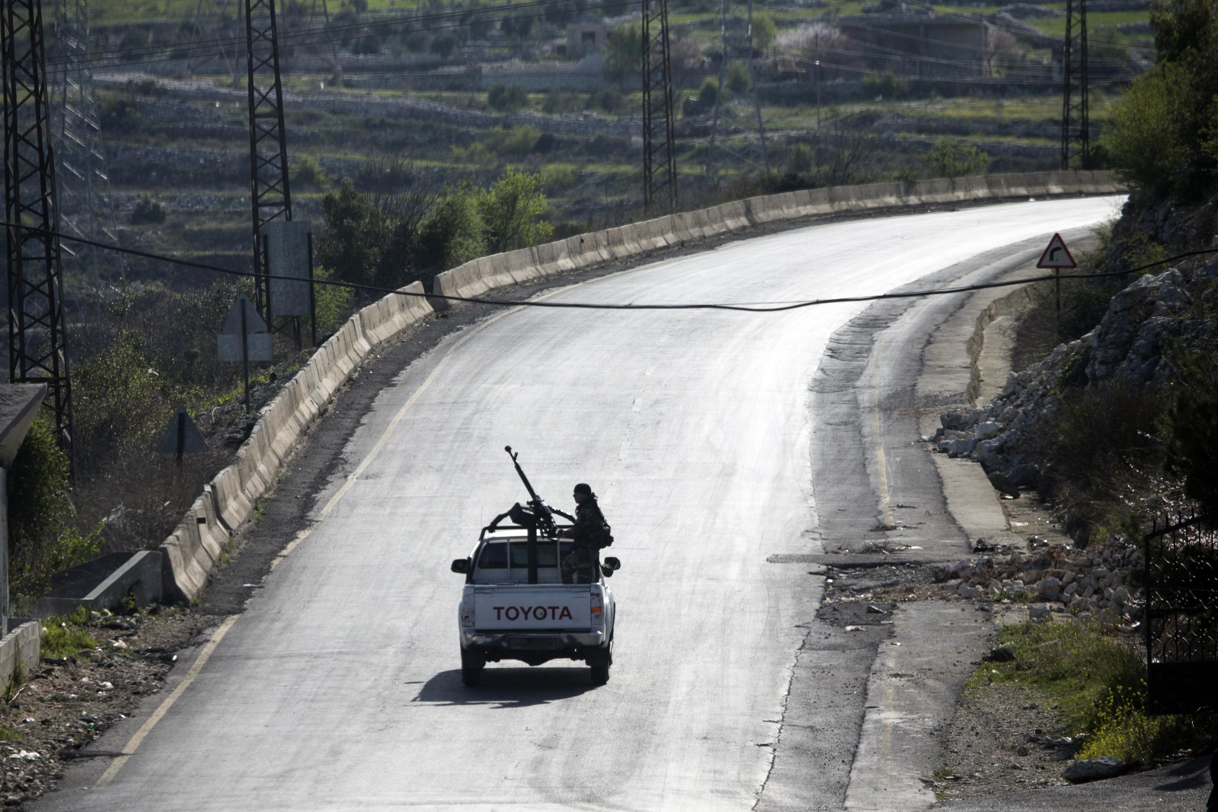 Syrian troops ride on a pickup truck with a mounted machine gun on a road near Latakia in Syria