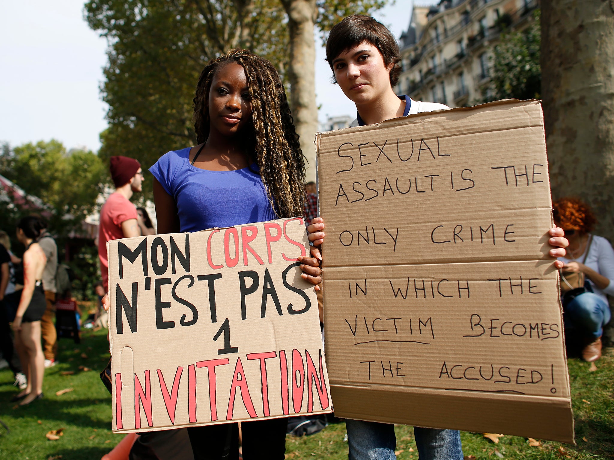 Two women attend a Paris protest against blaming victims of sexual violence. The sign on the left reads 'My body is not an invitation'