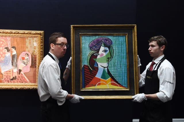 Staff members carry the painting 'Tete de Femme (1935)' by Spanish artist Pablo Piccaso next to French artist Henri Matisse's work 'La Lecon de Piano' during a press preview at Sotheby's auction house in London