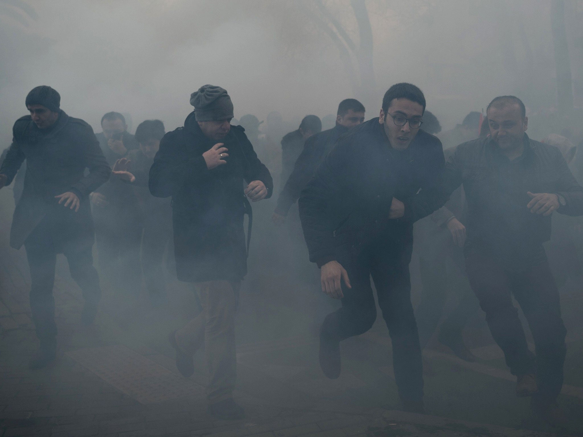 Men run as Turkish anti-riot police officers use tear gas to disperse supporters in front of the headquarters of the Turkish daily newspaper Zaman in Istanbul on March 5, 2016,