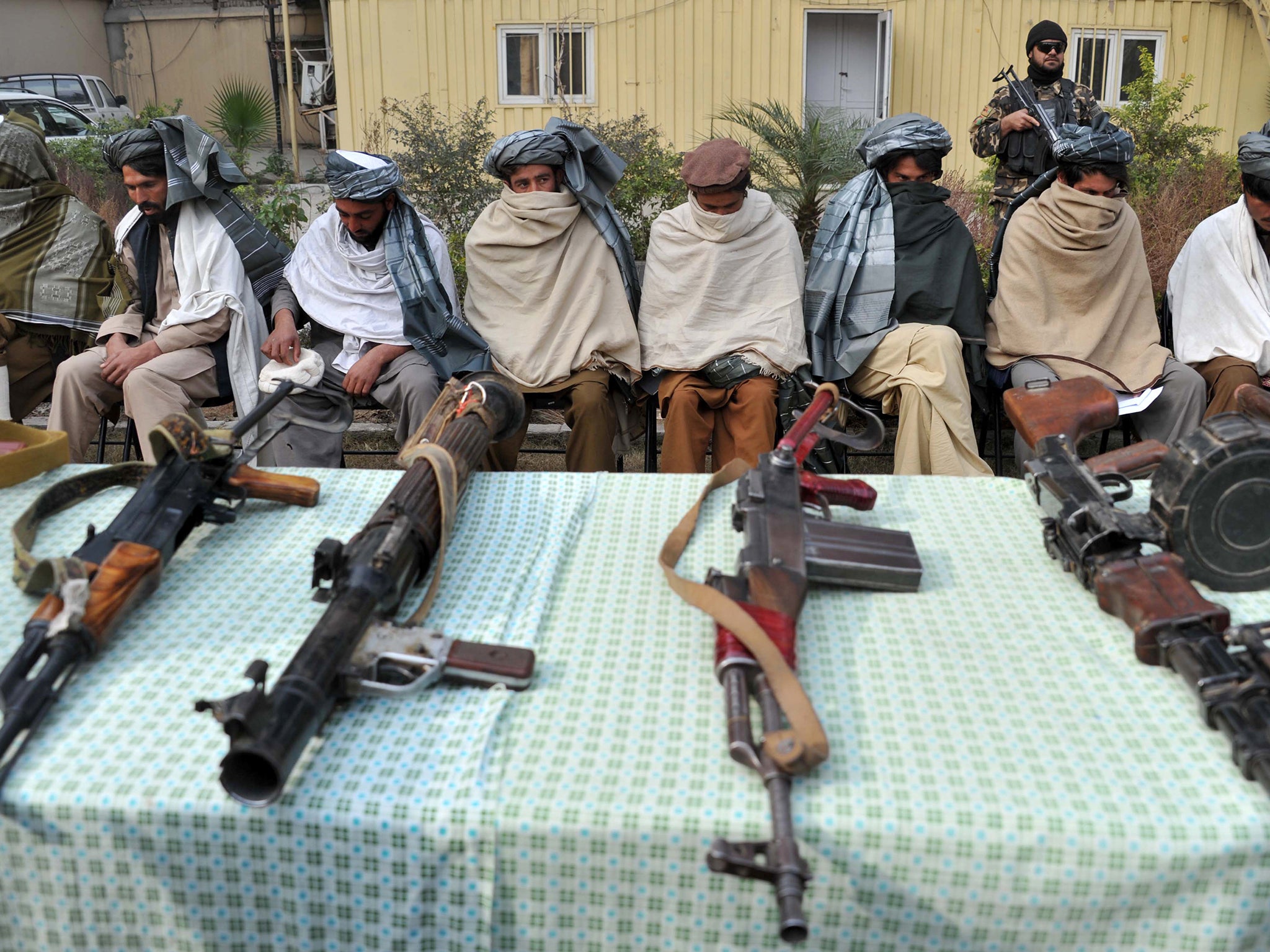 Former Taliban fighters sit alongside their weapons, prior to handing them over at a ceremony in Jalalabad in 2014