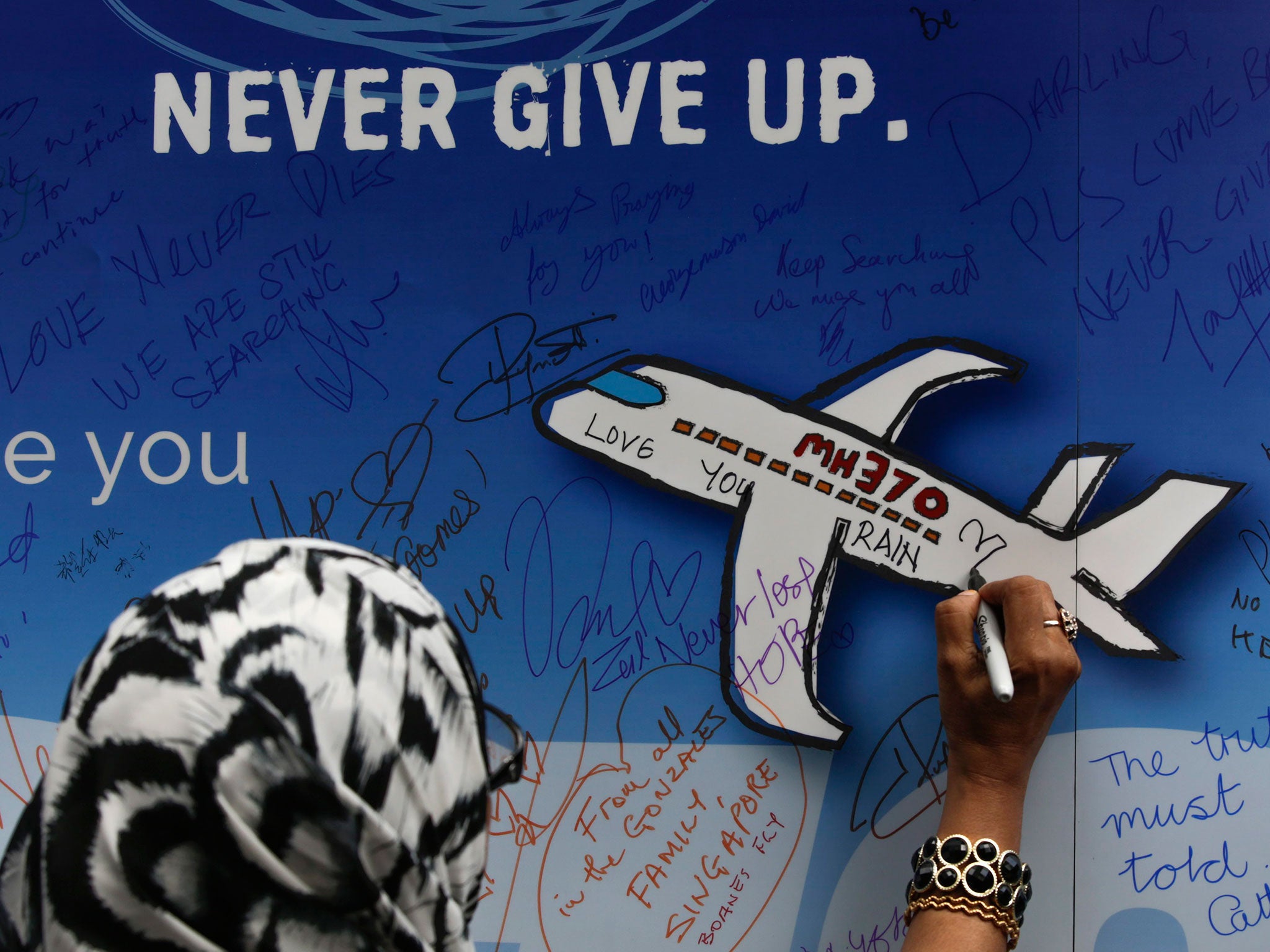 A woman writes messages for the passengers of flight MH370 on a banner during a remembrance ceremony to mark the second anniversary of the plane’s disappearance in Kuala Lumpur