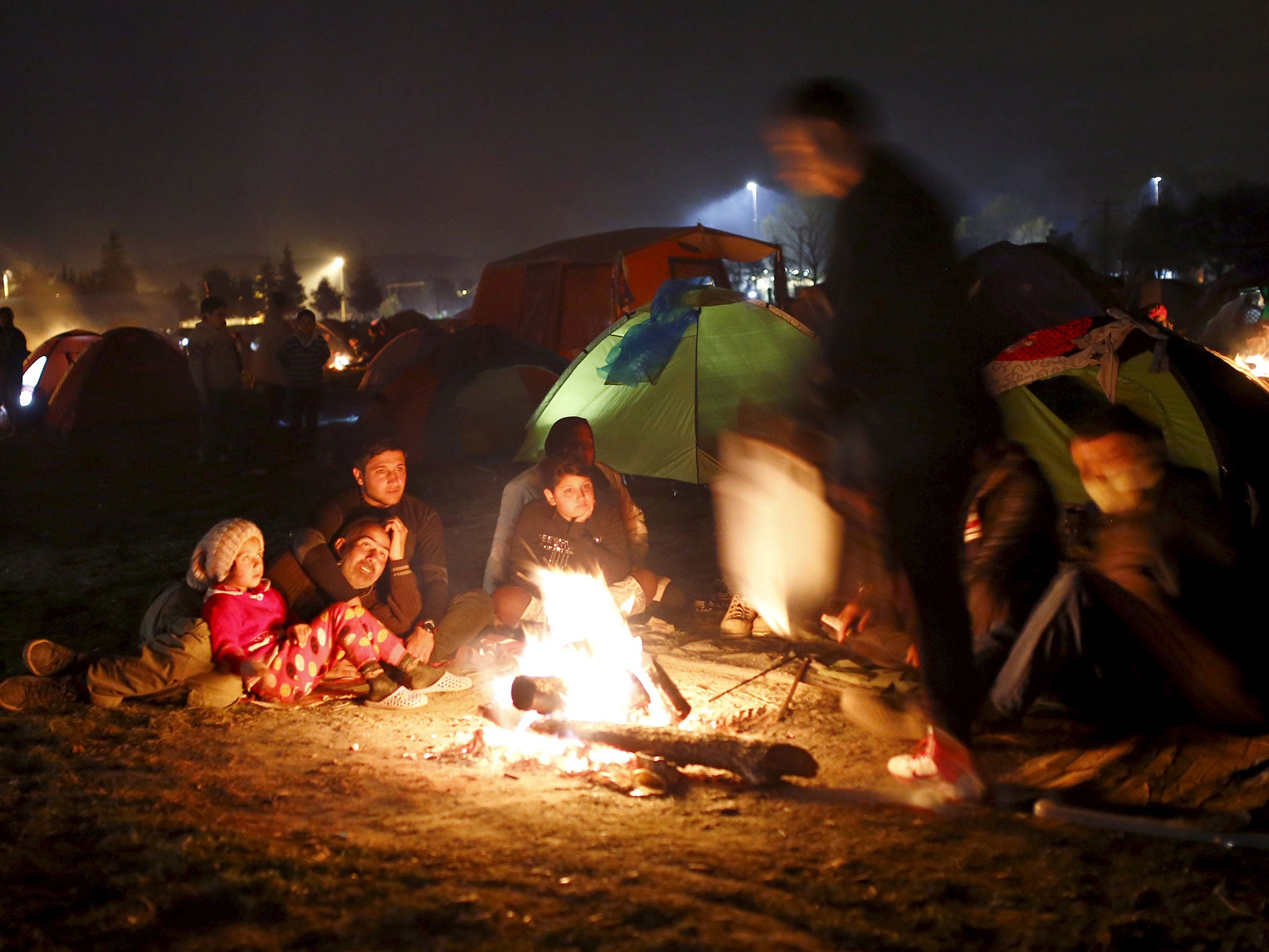 Migrants waiting to cross the Greek-Macedonian border warm themselves by a fire next to tents near the village of Idomeni, Greece