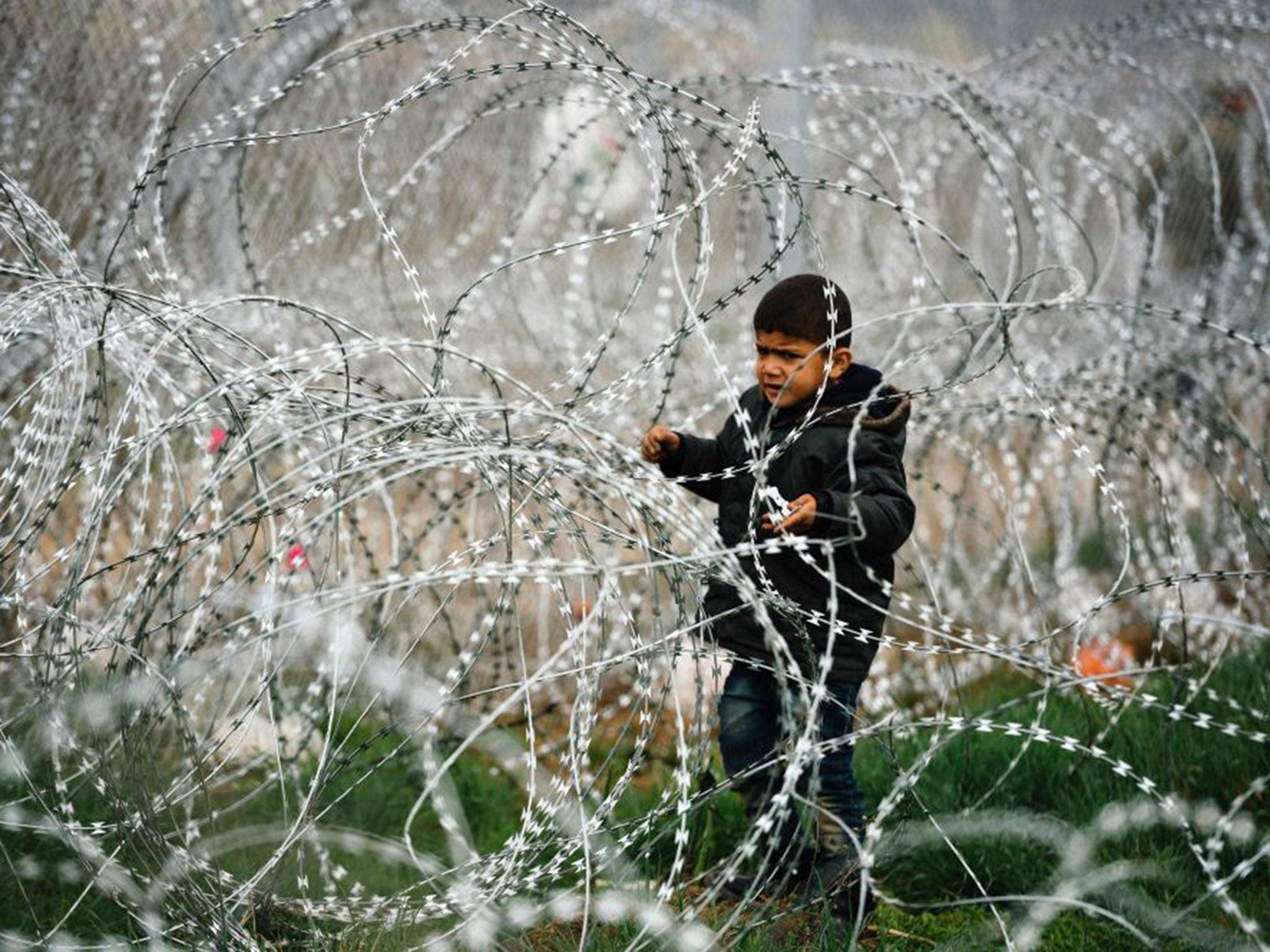 A child stands among razor-wire fencing on the Greek-Macedonian border near the Greek village of Idomeni