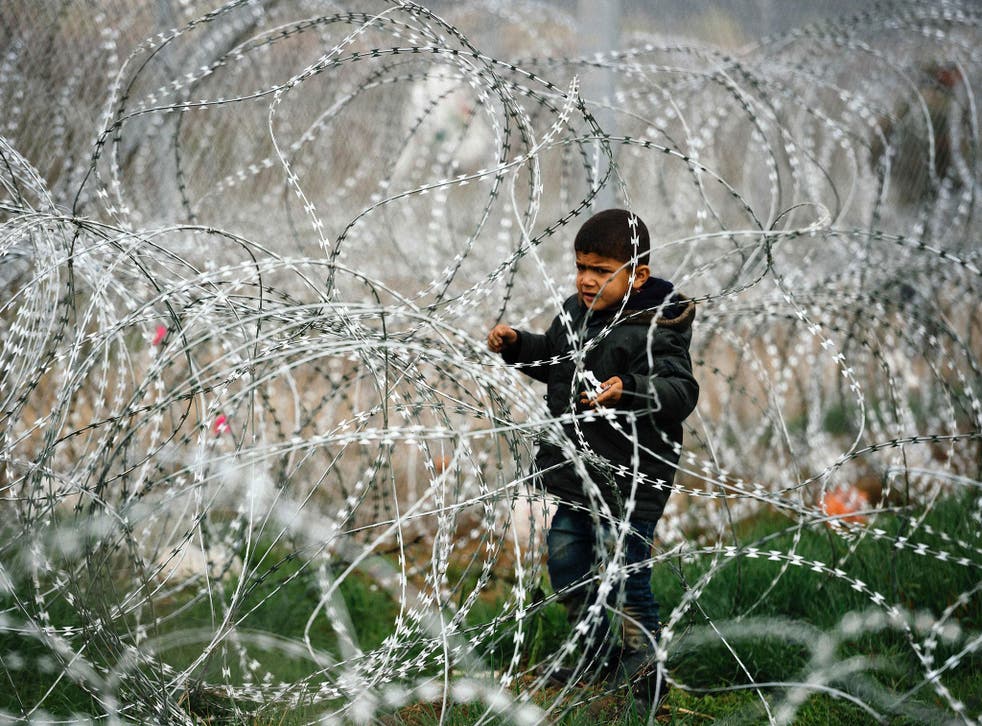 A child stands among a razor-topped fence close to the gate at the Greek-Macedonian border, 7 March 2016