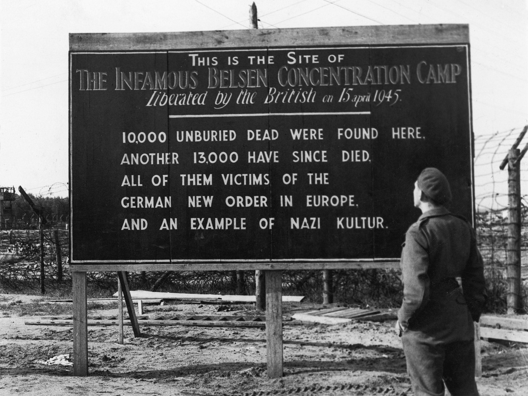 &#13;
A British soldier reads a billboard posted at the entrance of the Belsen concentration camp (Getty)&#13;