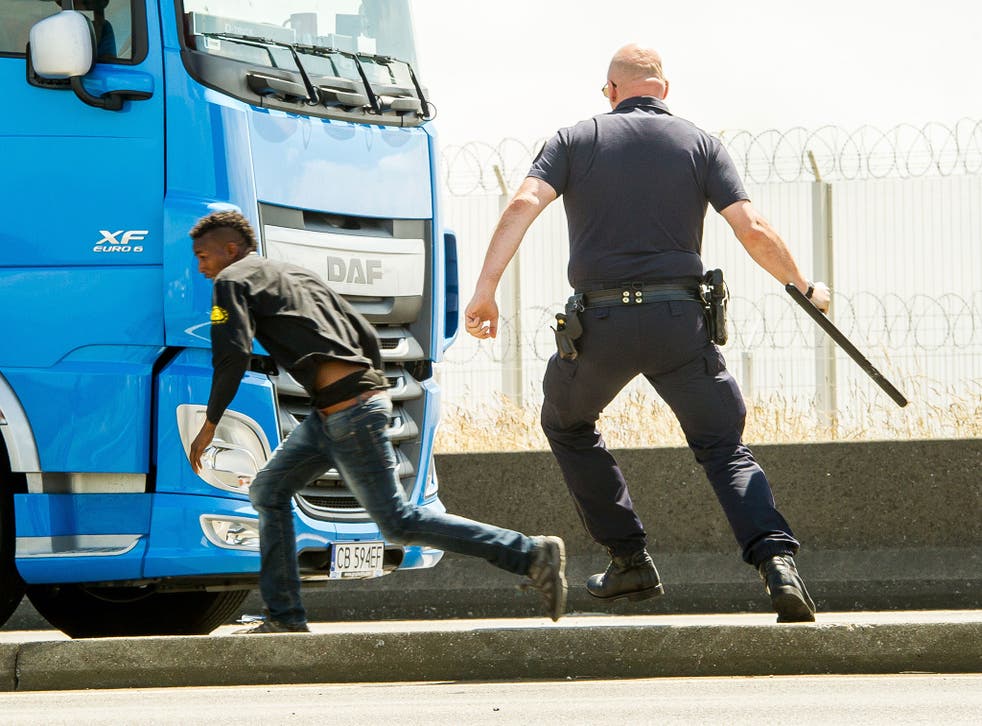 French police (CRS) officer runs after a migrant trying to hide in a lorry heading for England in Calais on June 17, 2015.