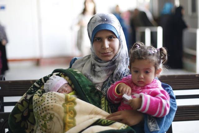 Syrian refugee Kholod carries her daughters Fedaa’, right, and Rima at Zaatari refugee camp in Jordan