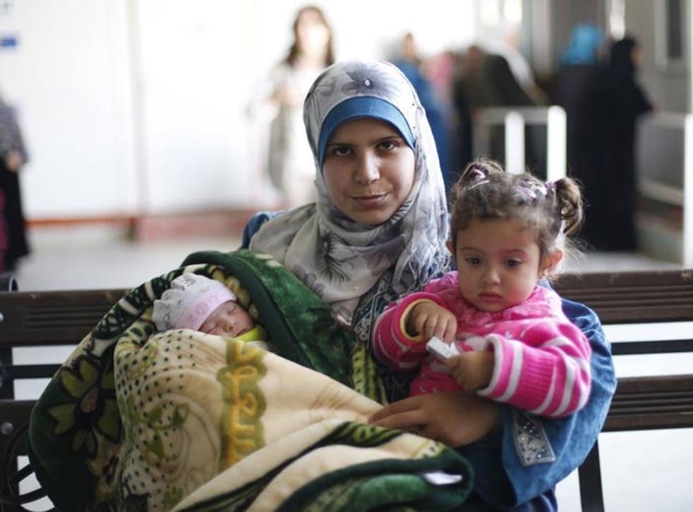 Syrian refugee Kholod carries her daughters Fedaa’, right, and Rima at Zaatari refugee camp in Jordan