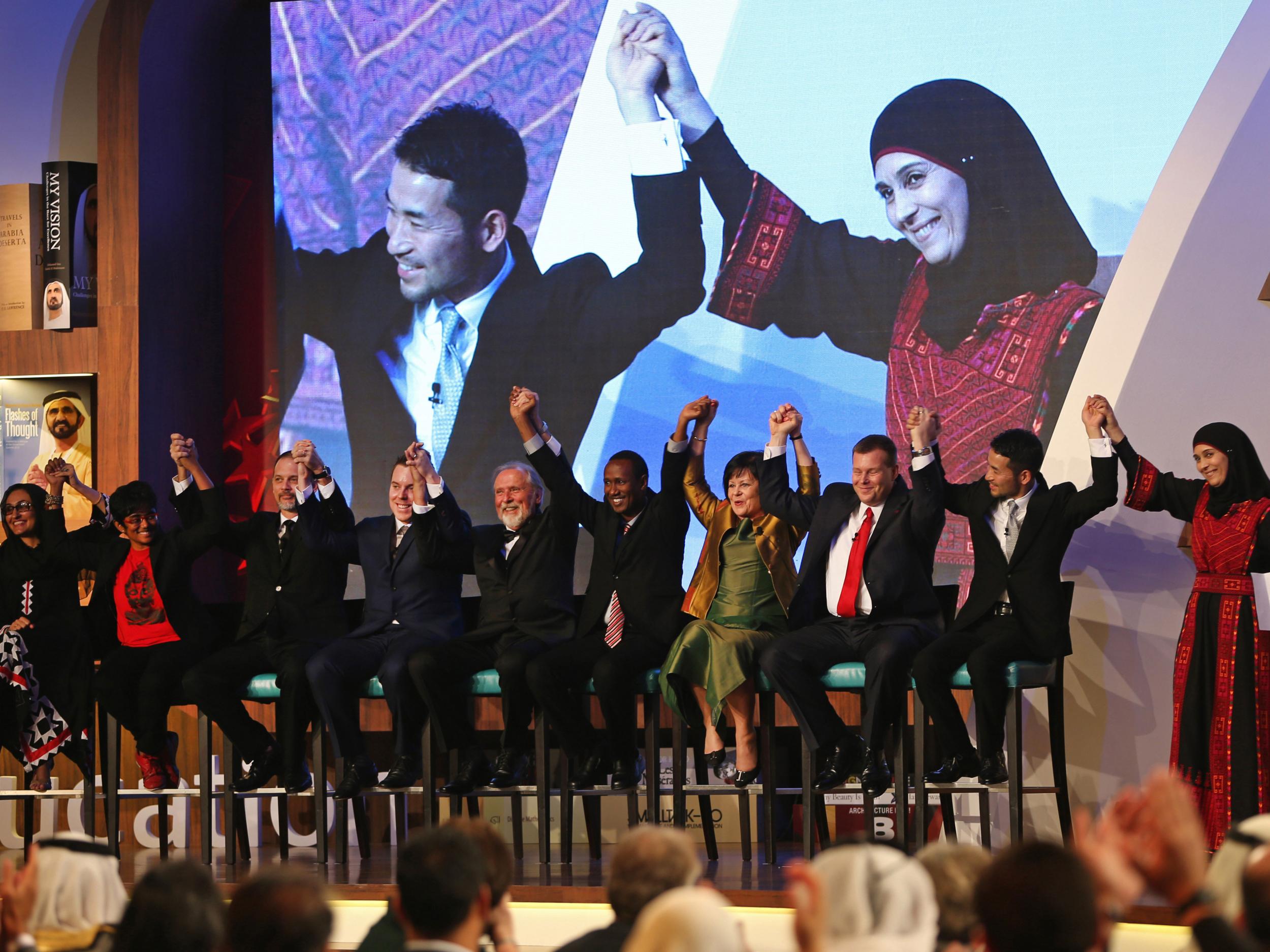 Hanan al-Hroub, right and right on screen at top, raises hands with the other finalists after she won the second annual Global Teacher Prize