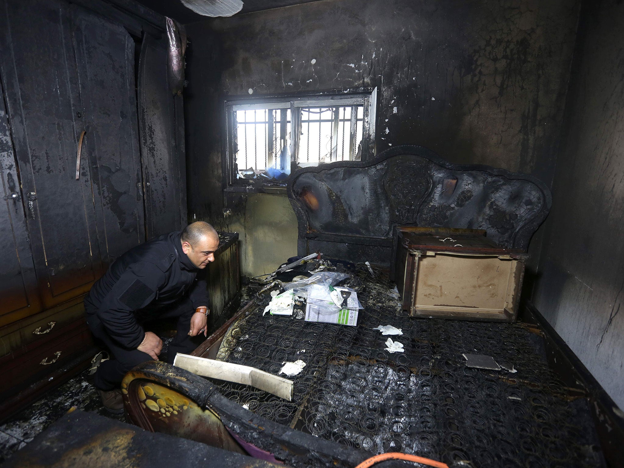 A Palestinian police member inspects the damage inside a burnt-out house belonging to a key witness to an arson attack