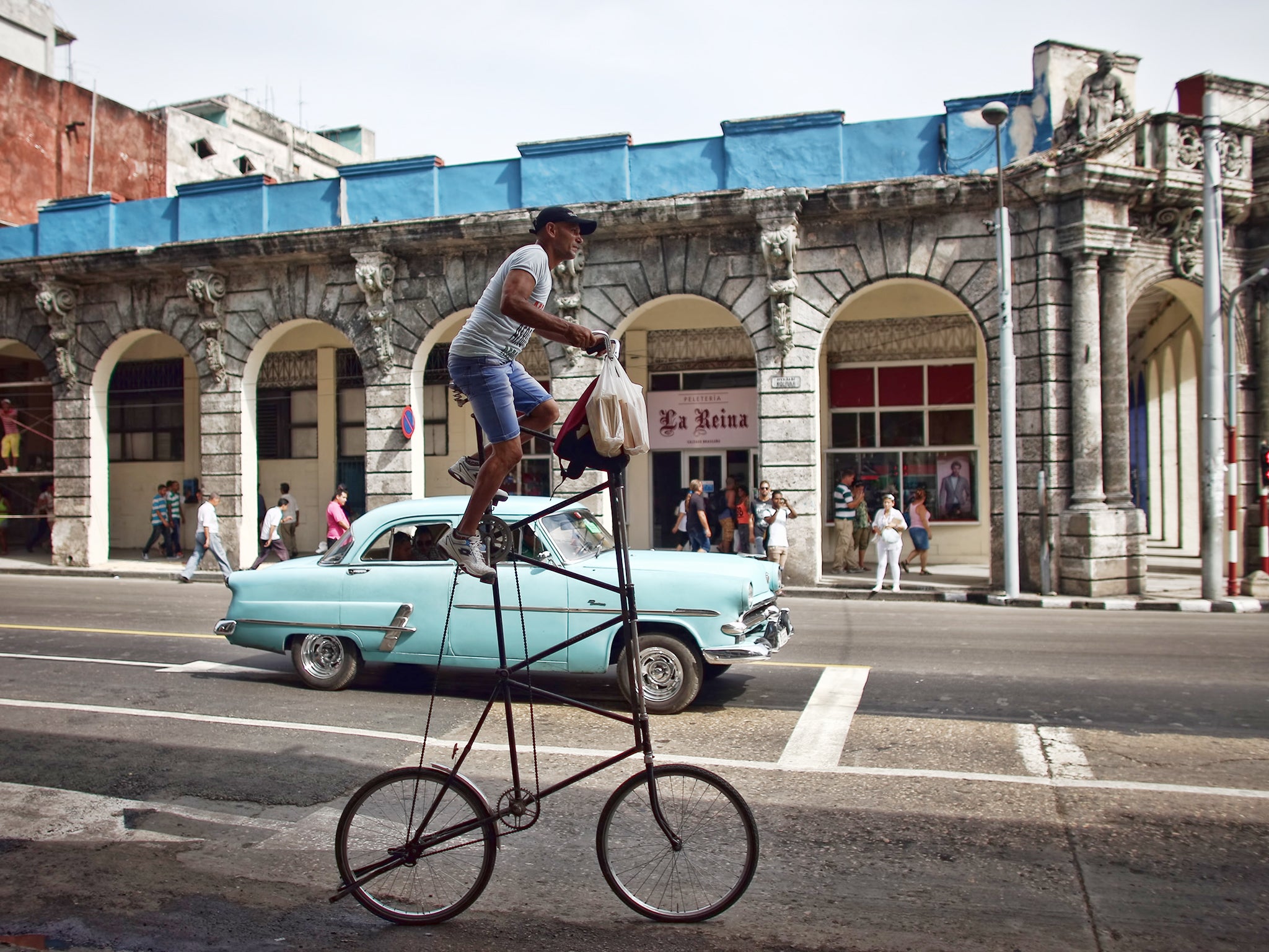 A man rides his modified bicycle past a vintage American car in Havana