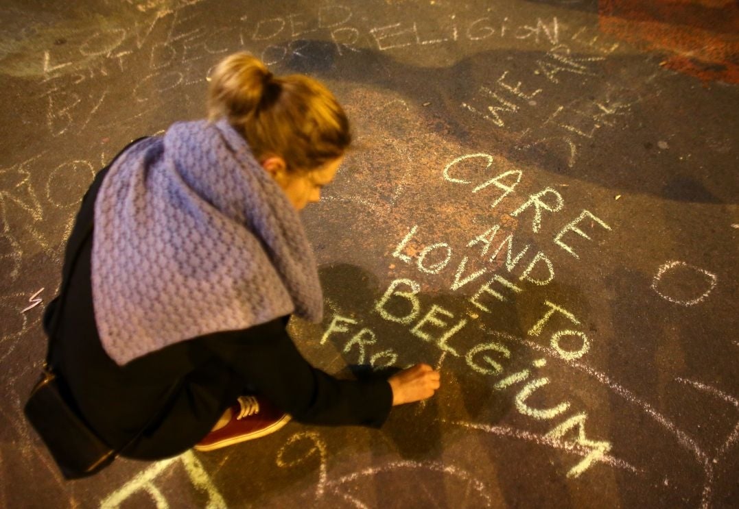 A woman writes a message on the ground as people leave tributes at the Place de la Bourse following today's attacks on March 22, 2016 in Brussels, Belgium