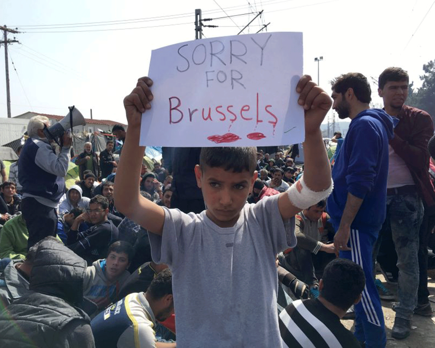 A boy holds a sign expressing sorrow for Brussels' deaths at the notorious Idomeni camp in Greece
