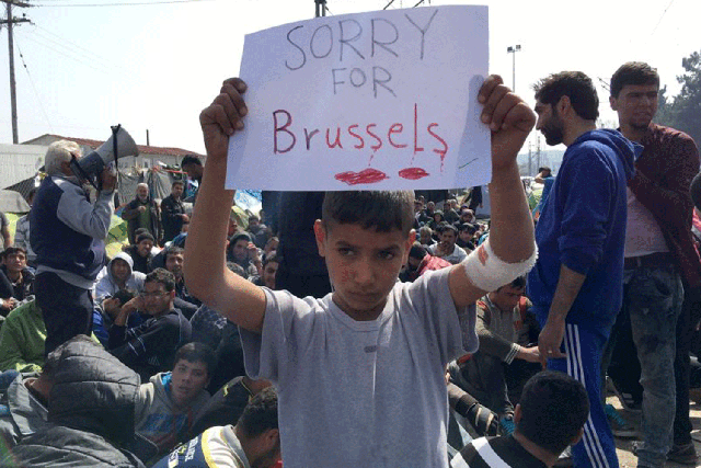 A boy holds a sign expressing sorrow for Brussels' deaths at the notorious Idomeni camp in Greece