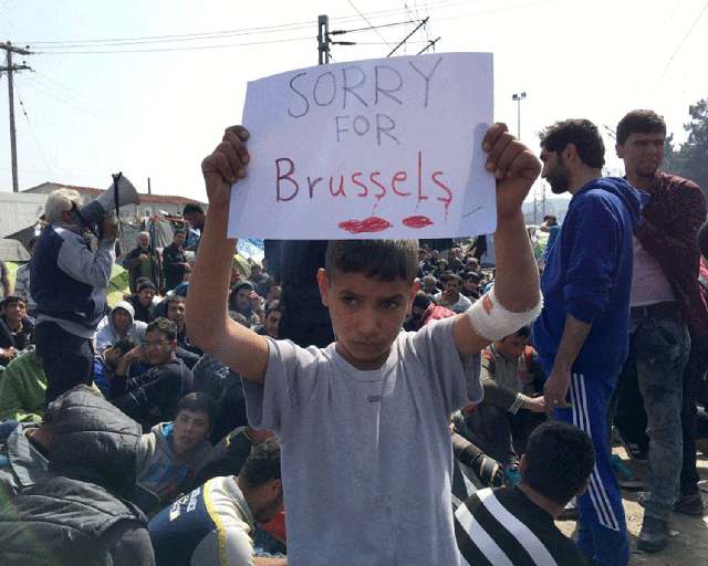 A boy holds a sign expressing sorrow for Brussels' deaths at the notorious Idomeni camp in Greece