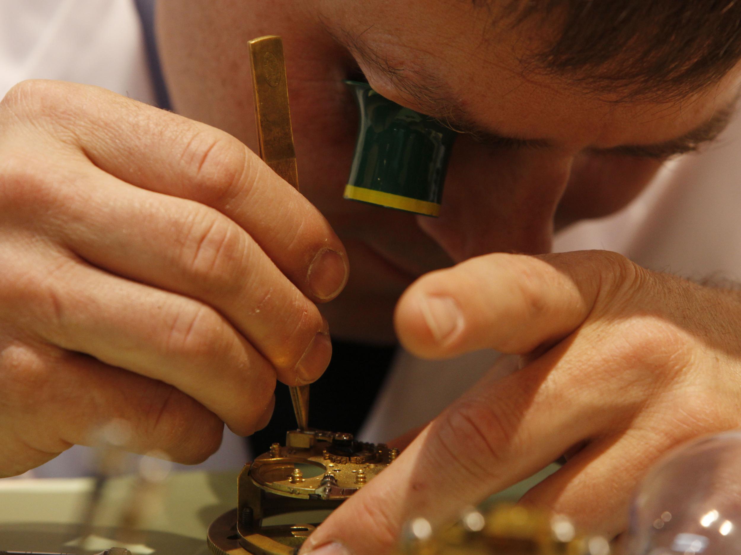 A watchmaker works on a watch mechanism at the Baselworld trade show in Basel, Switzerland