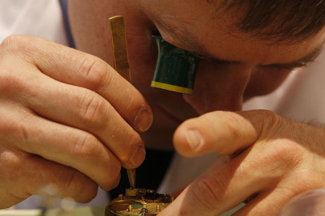 A watchmaker works on a watch mechanism at the Baselworld trade show in Basel, Switzerland