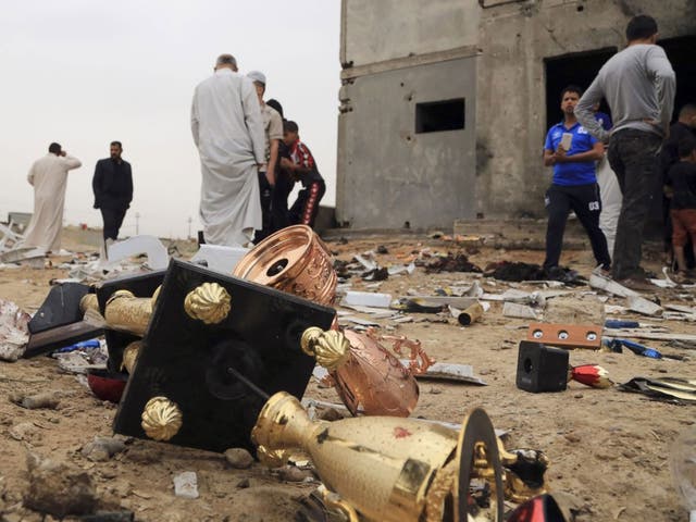 Broken trophies lie on the ground as people inspect the aftermath of a suicide bombing at a small football stadium in Iskandariya