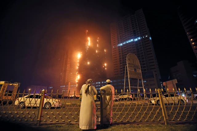 Two Emirati officials watch a high-rise building as a fire spreads up the side of the building in Ajman, United Arab Emirates