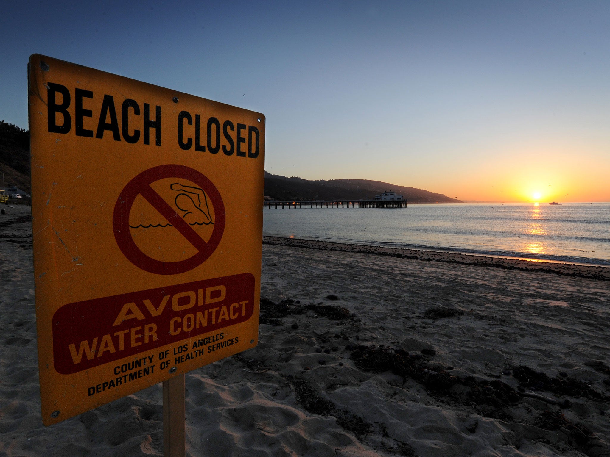 A beach closed sign warns against contaminated water