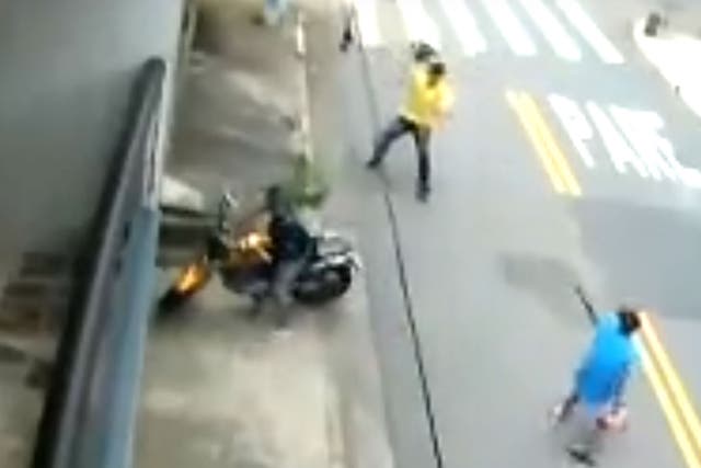 The man fends off the gun-wielding attacker with his crash helmet
